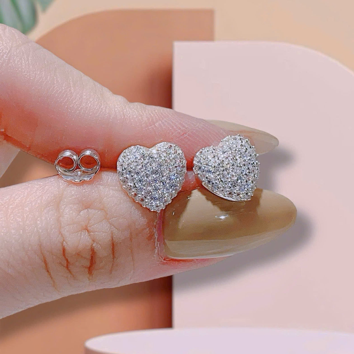 Heart-shaped earrings being held between fingers with a neutral background