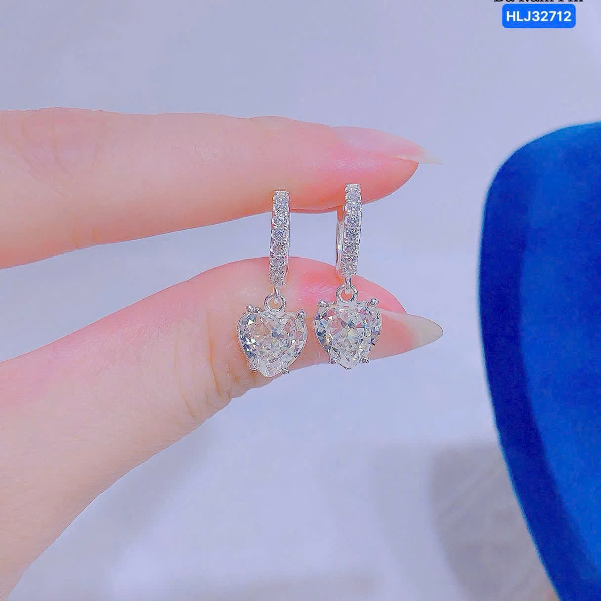 Heart-shaped earrings held between fingers against a light background