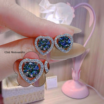 Heart-shaped gemstone earrings held by a hand with a blurred background