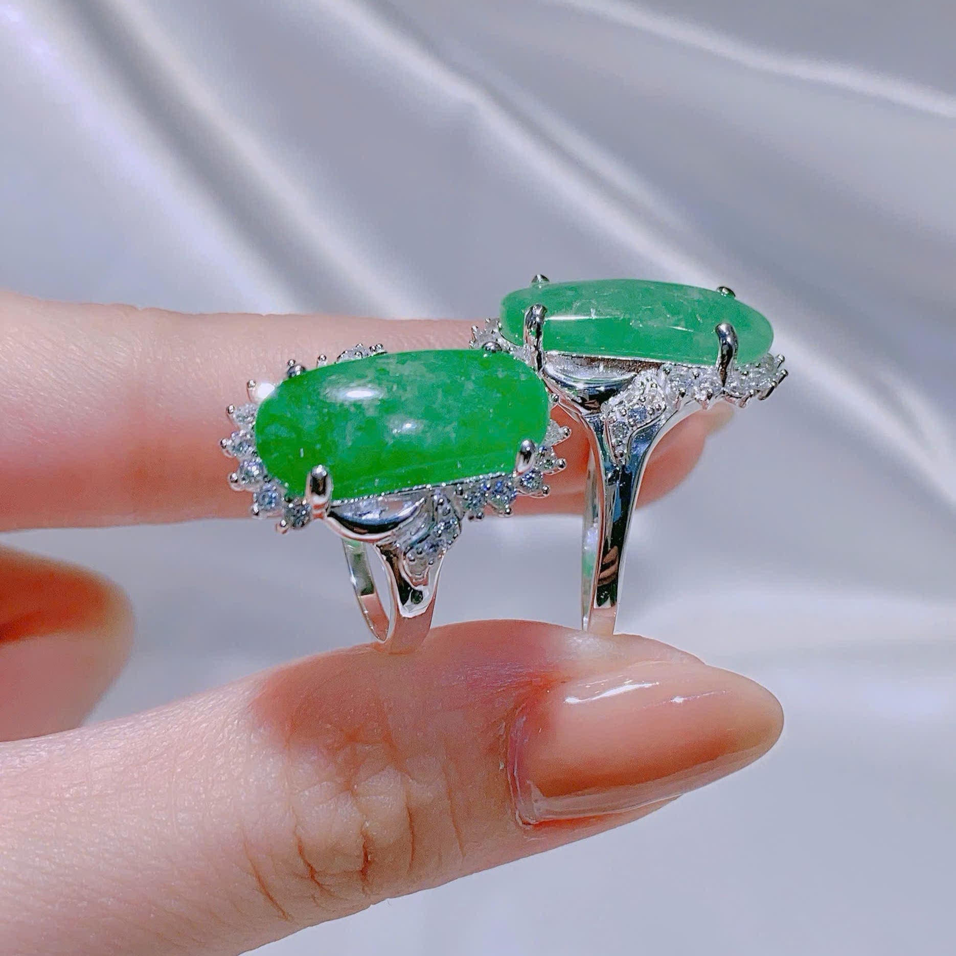 Jewelry with green gemstones held between fingers against a neutral background