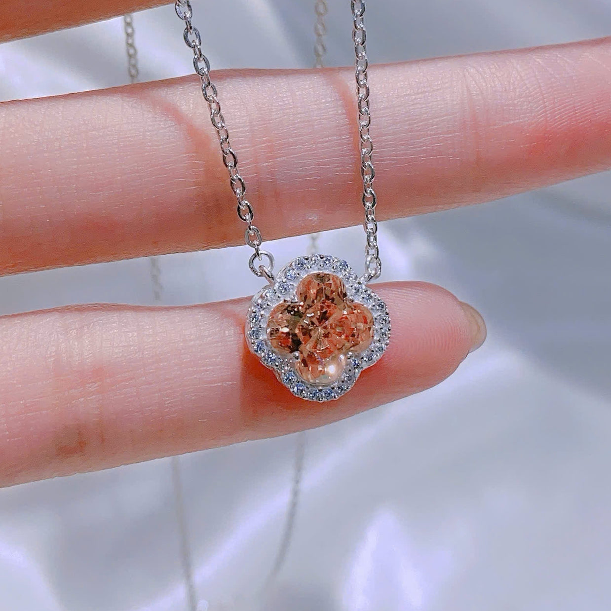 Necklace with a floral pendant held between fingers against a blurred background