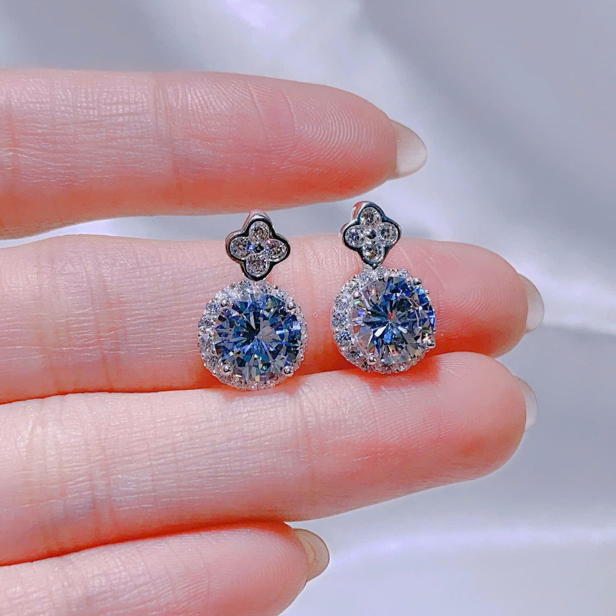 Pair of blue gemstone earrings held between two fingers against a neutral background