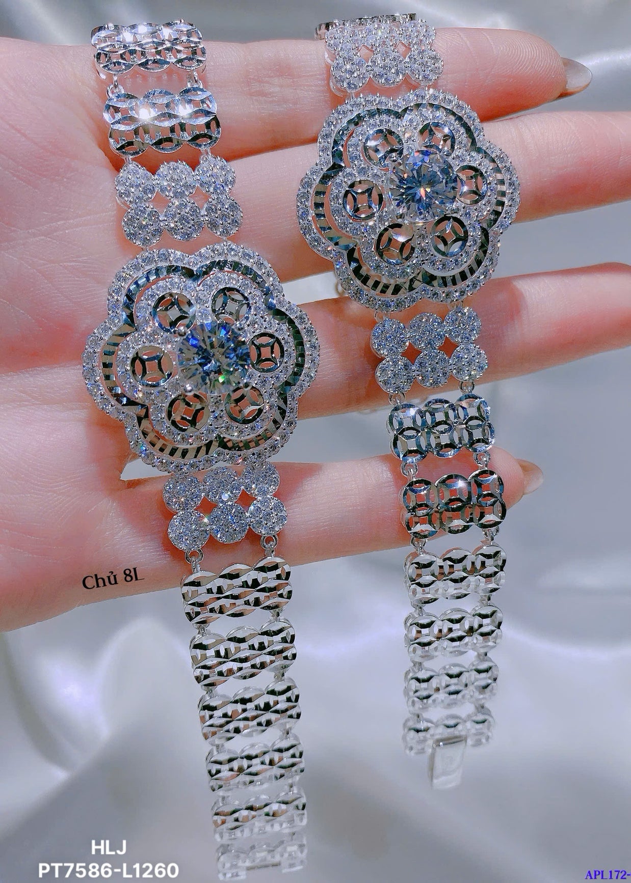 Pair of silver floral earrings held between fingers on a neutral background