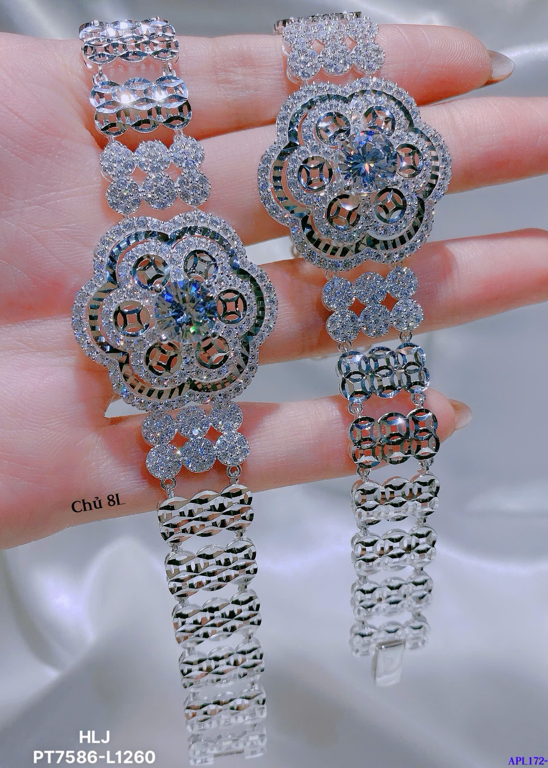 Pair of silver floral earrings held between fingers on a neutral background