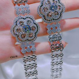 Pair of silver floral earrings held between fingers on a neutral background