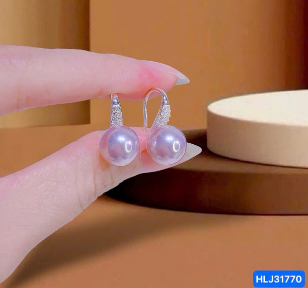 Pearl earrings held by a hand against a brown background