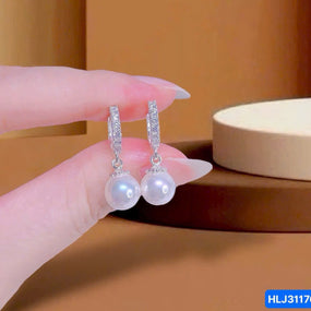 Pearl earrings held by a hand against a brown background