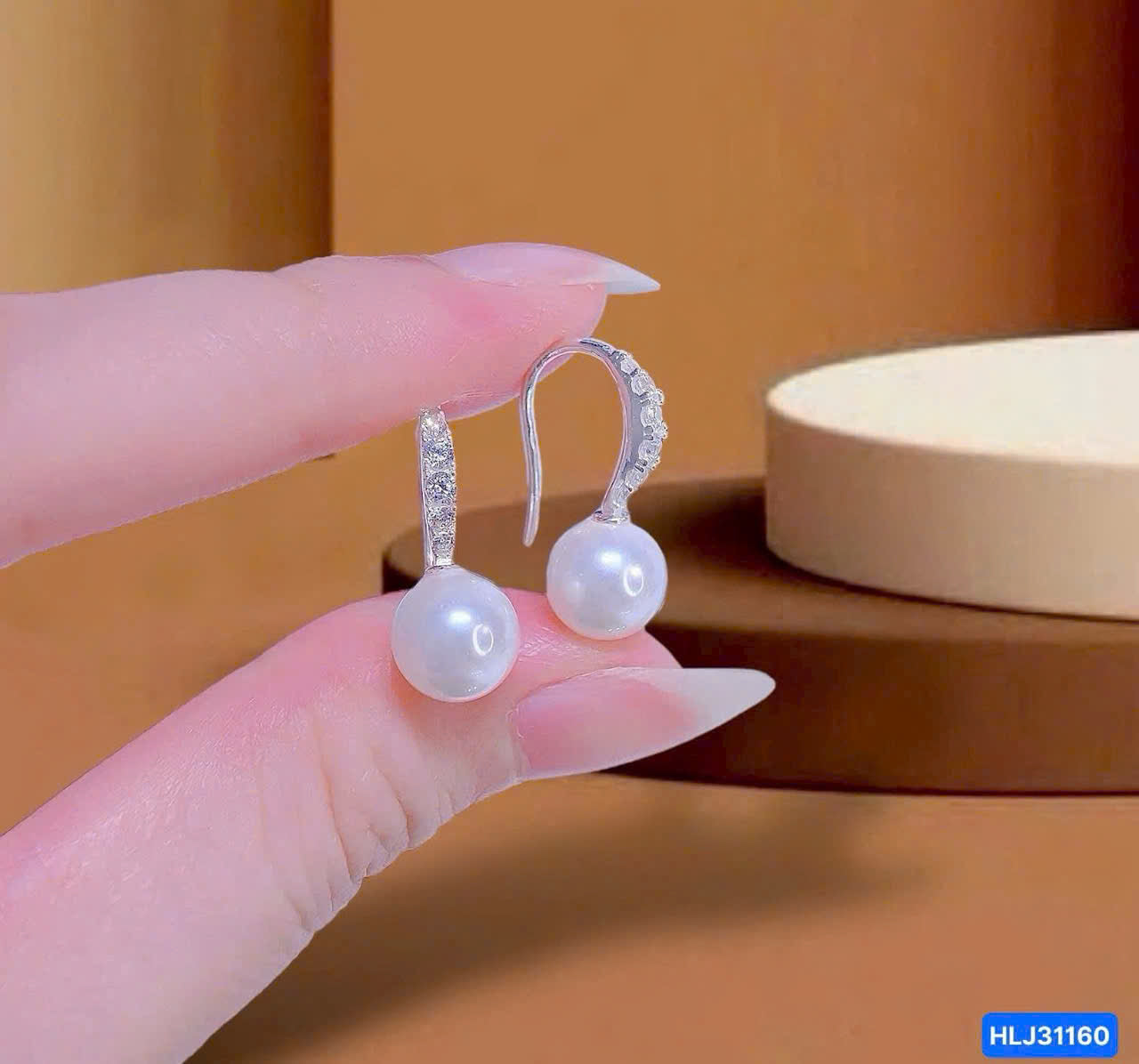 Pearl earrings held by a hand against a brown background