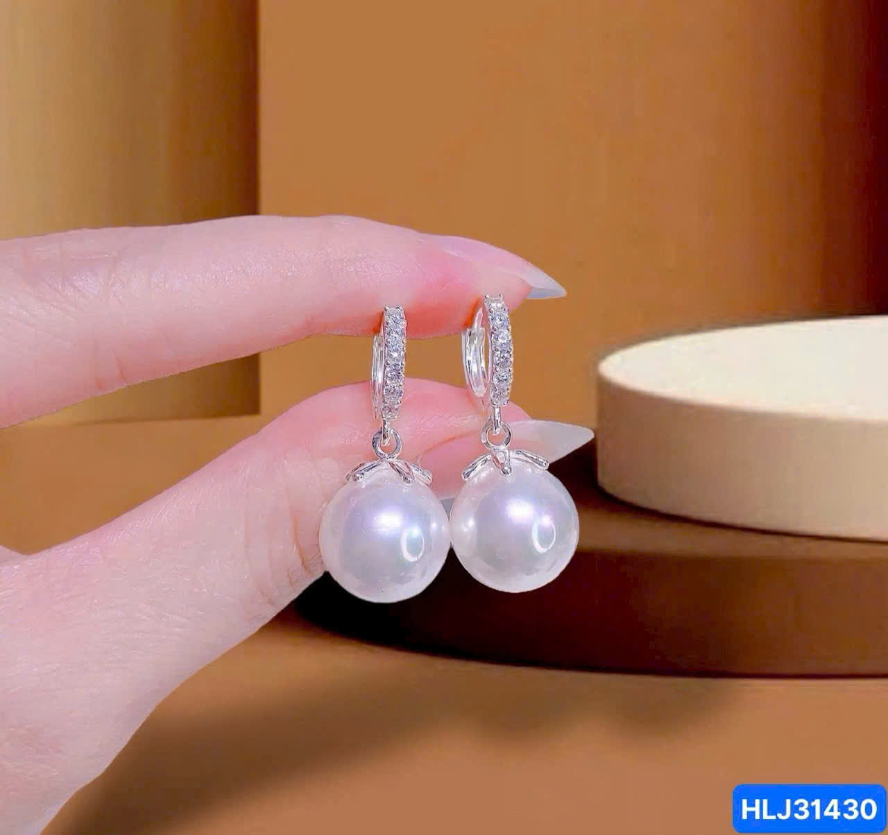 Pearl earrings held by a hand with a neutral background