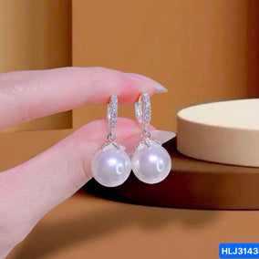 Pearl earrings held by a hand with a neutral background