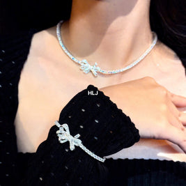Person wearing a silver necklace with a bow design, set against a black background.