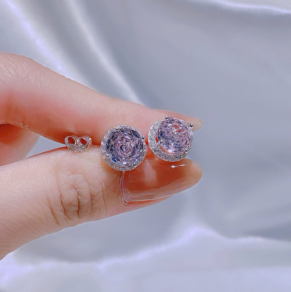 Pink gemstone earrings held between fingers against a neutral background