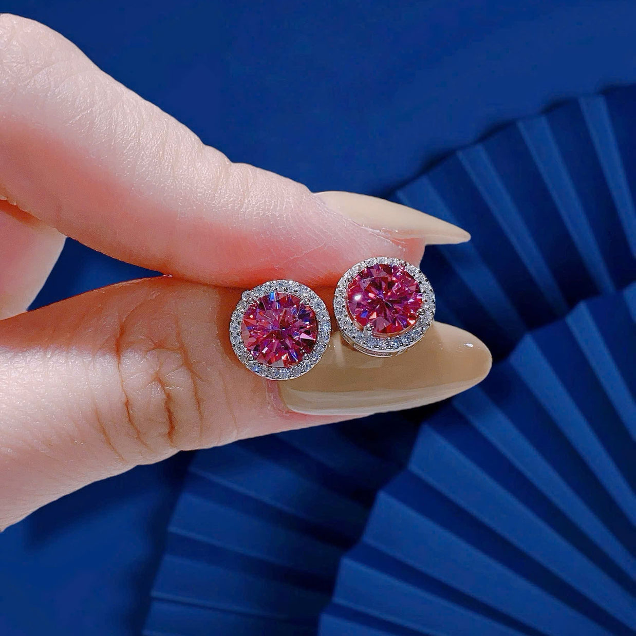Pink gemstone earrings held by a hand against a blue background