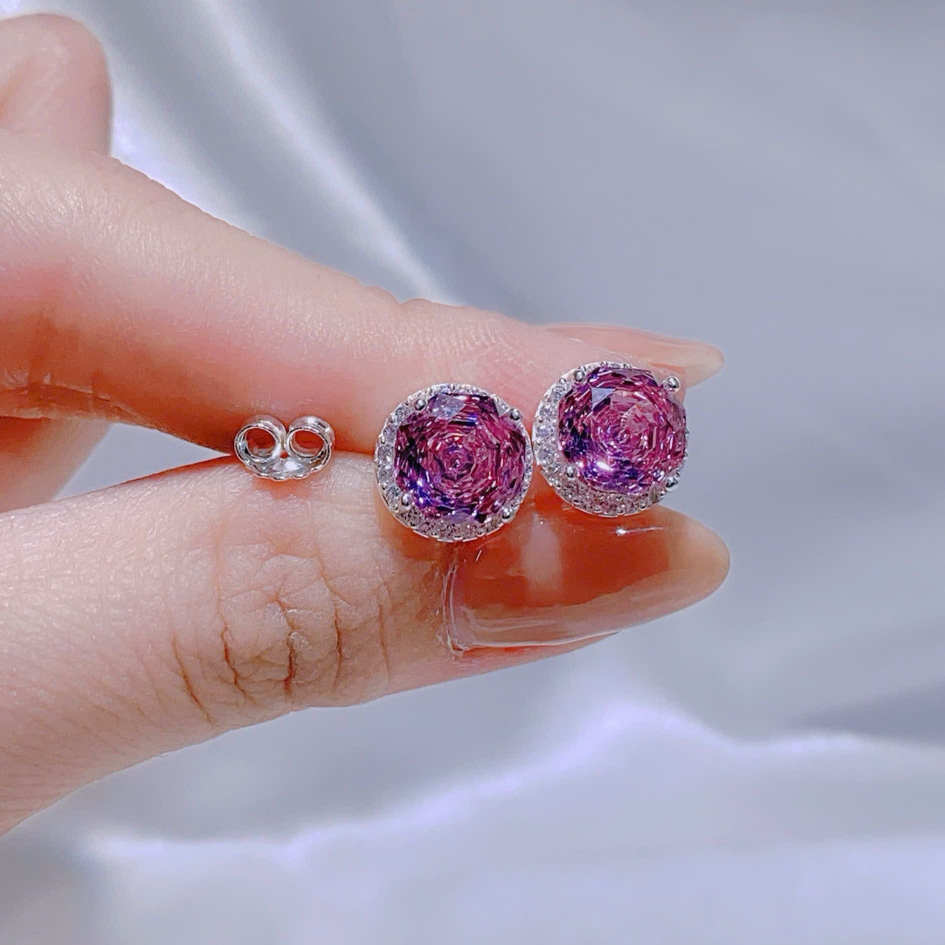 Pink gemstone earrings held by a hand against a light gray background