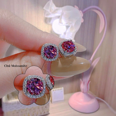 Pink gemstone earrings held by a hand with a blurred background