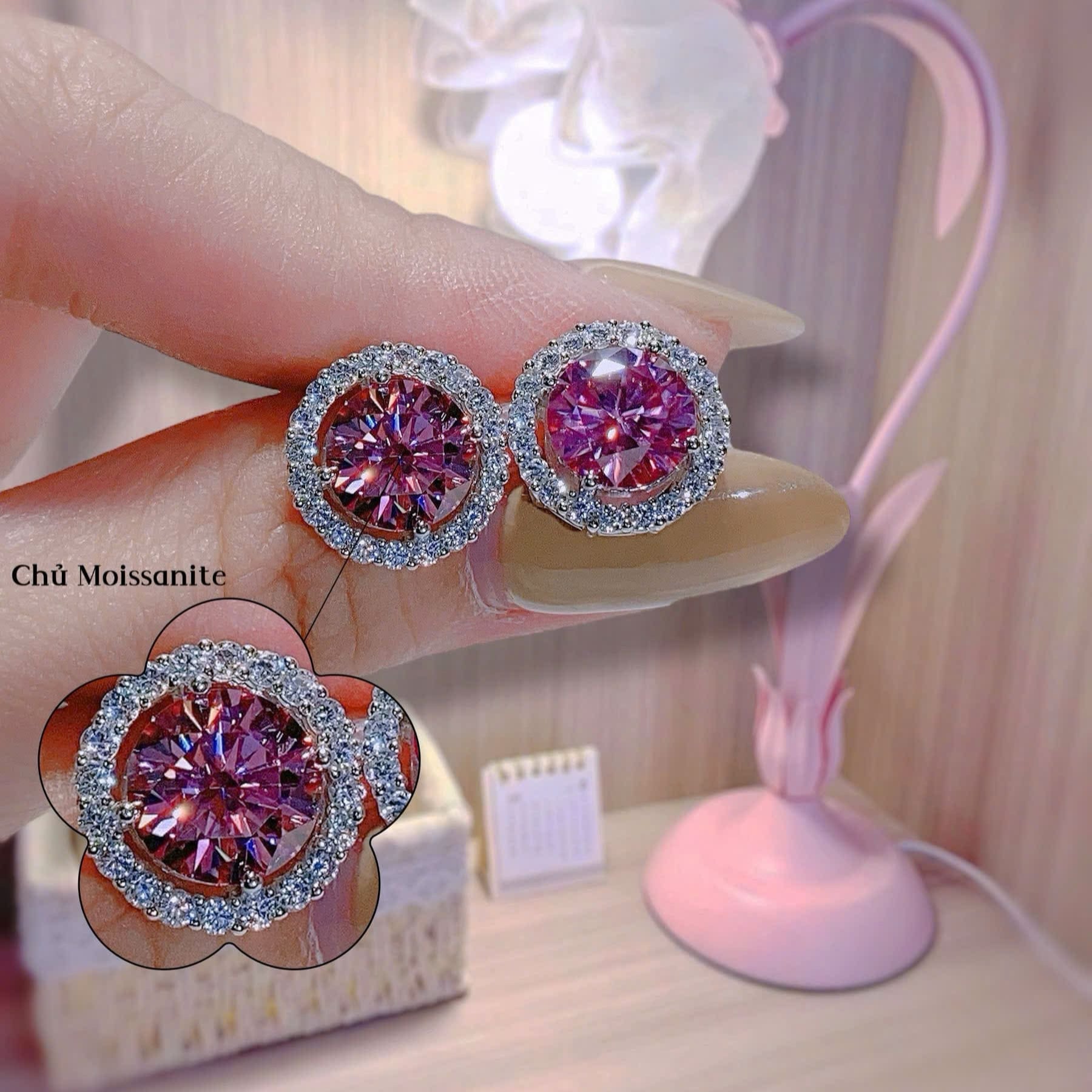 Pink gemstone earrings held by a hand with a blurred background
