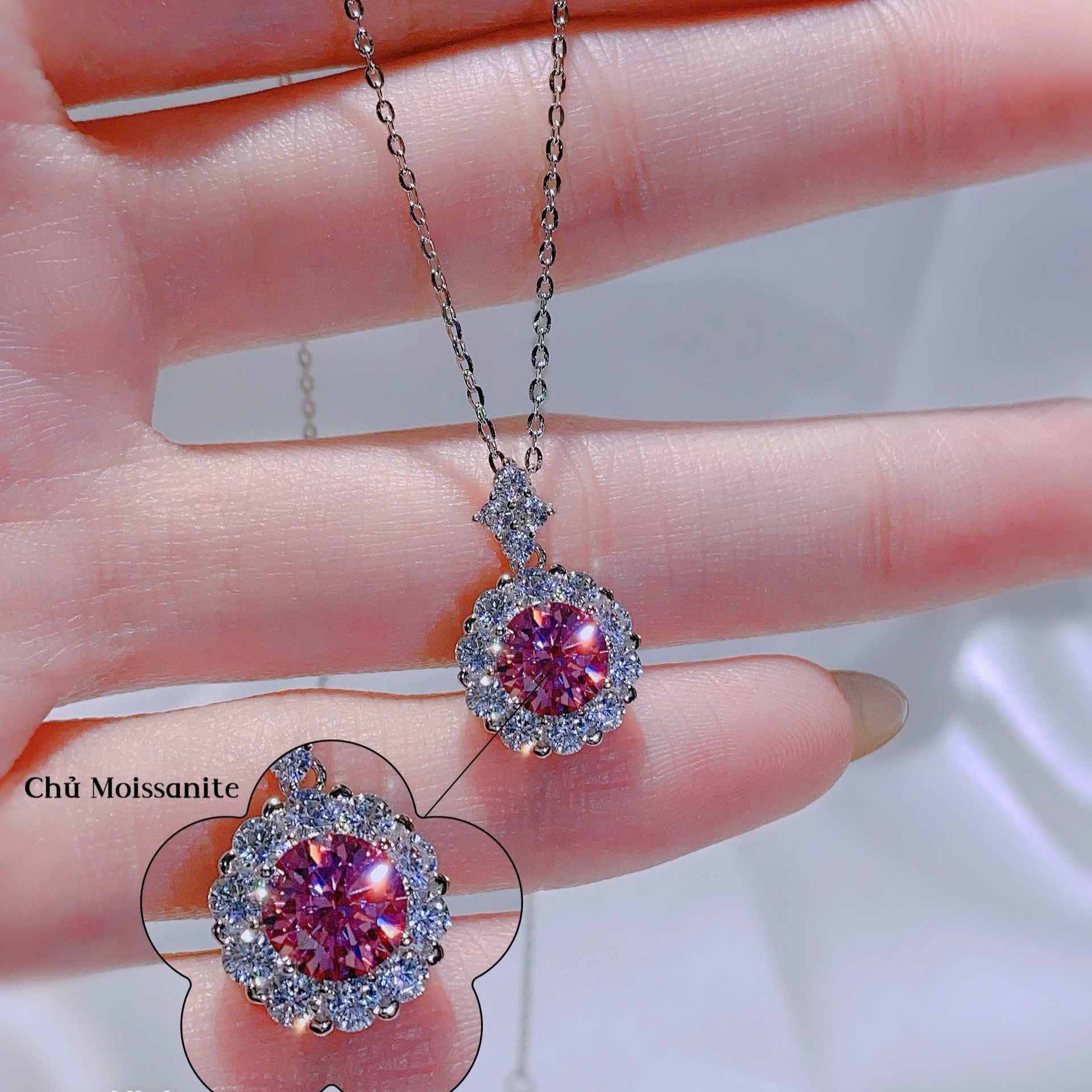 Pink gemstone pendant on a chain held between fingers with close-up inset.