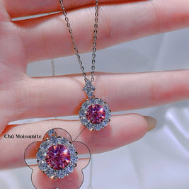 Pink gemstone pendant on a chain held between fingers with close-up inset.