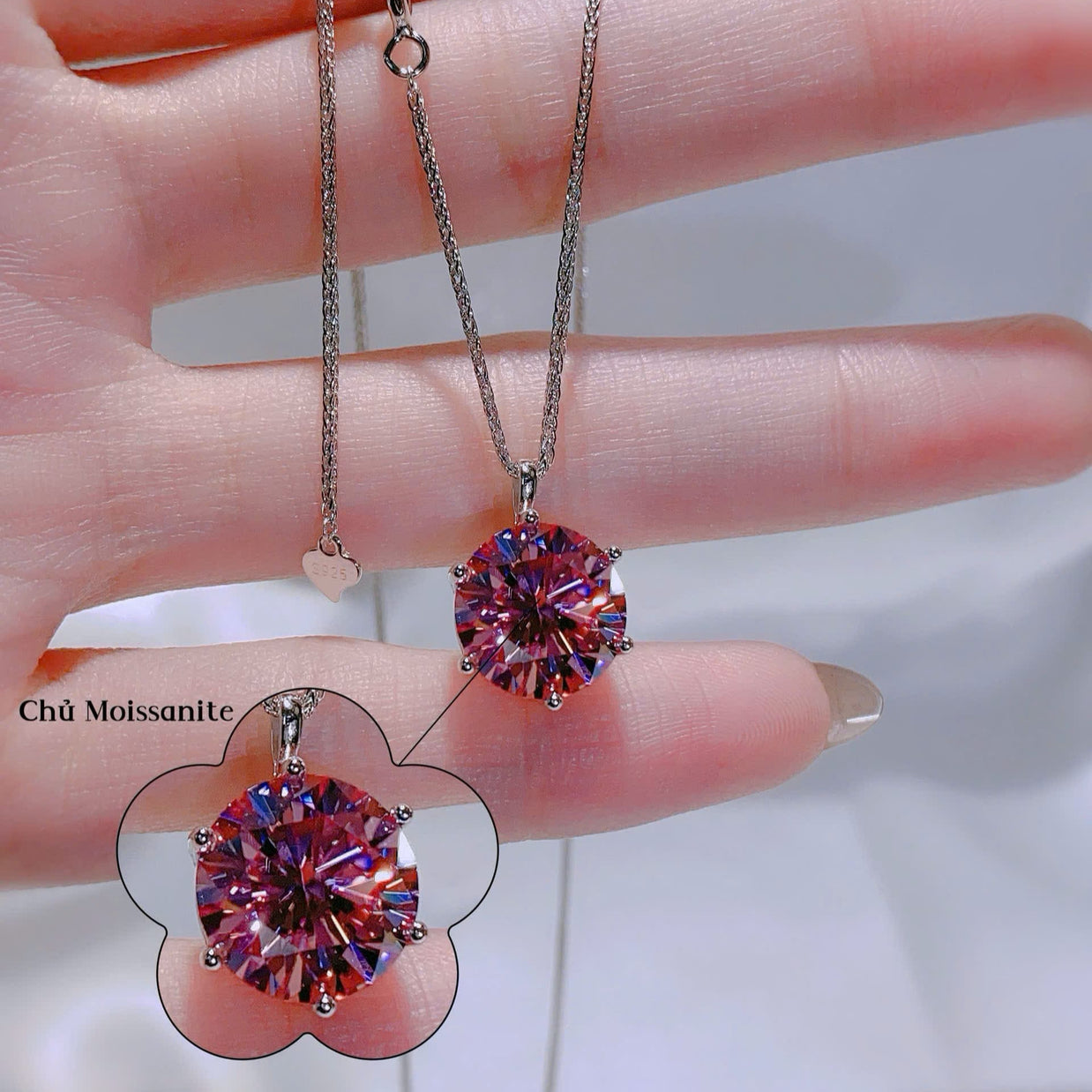 Pink gemstone pendant on a chain held by a hand with a blurred background