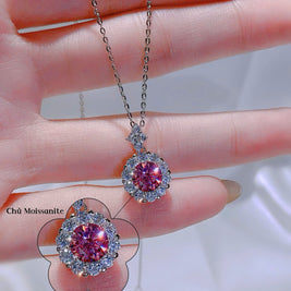Pink gemstone pendants on a chain held by a hand with a blurred background