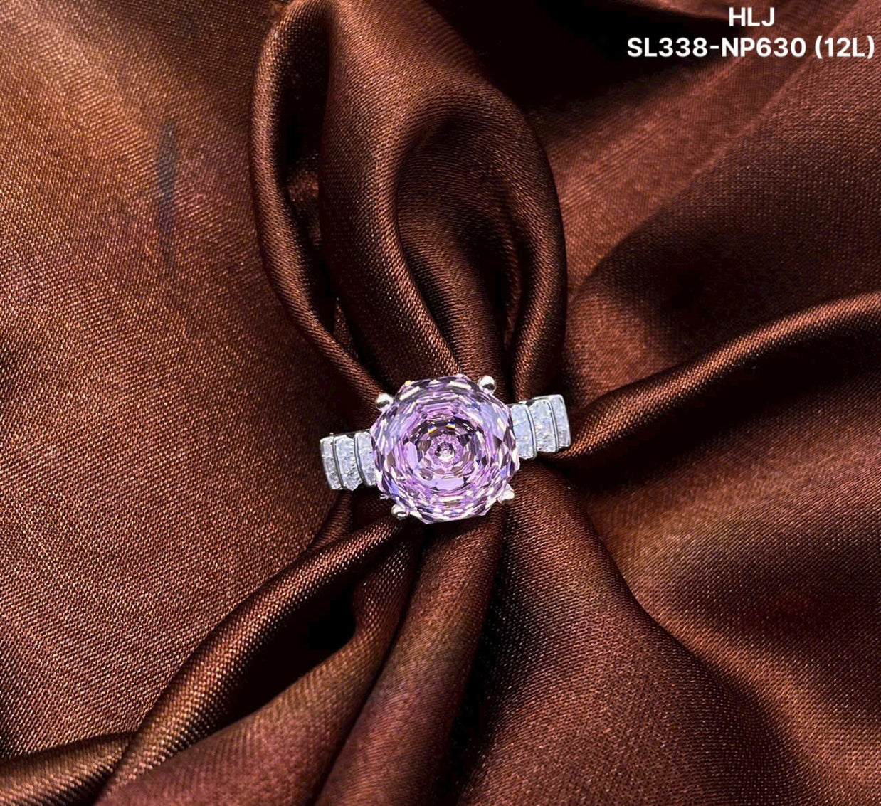 Pink gemstone ring with silver band on brown fabric, brand 'HLJ' visible