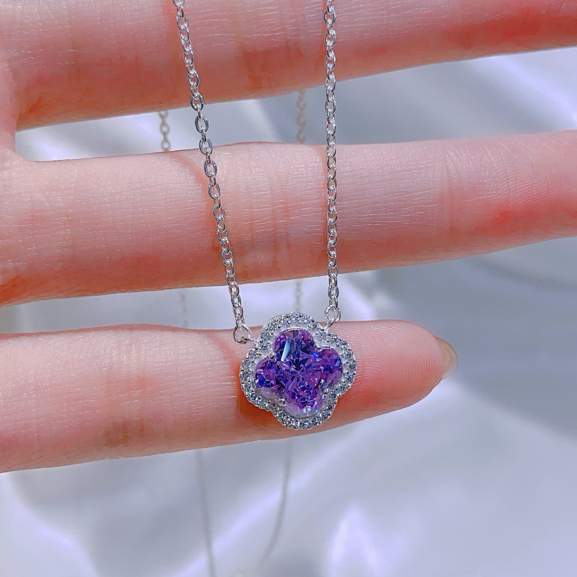 Purple heart-shaped pendant on a silver chain held between fingers