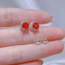 Red gemstone earrings held between fingers with a blurred background