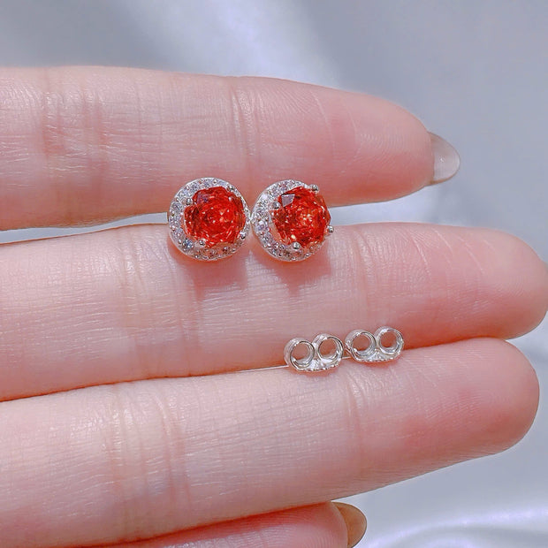 Red gemstone earrings held between fingers with a blurred background