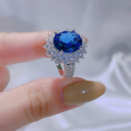 Ring with a blue gemstone held between fingers against a blurred background