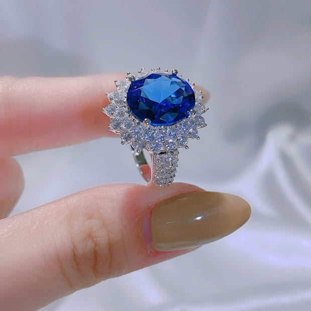 Ring with a blue gemstone held between fingers against a blurred background