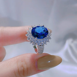 Ring with a blue gemstone held by a hand against a blurred background