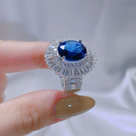 Ring with a blue gemstone held by a hand against a white background