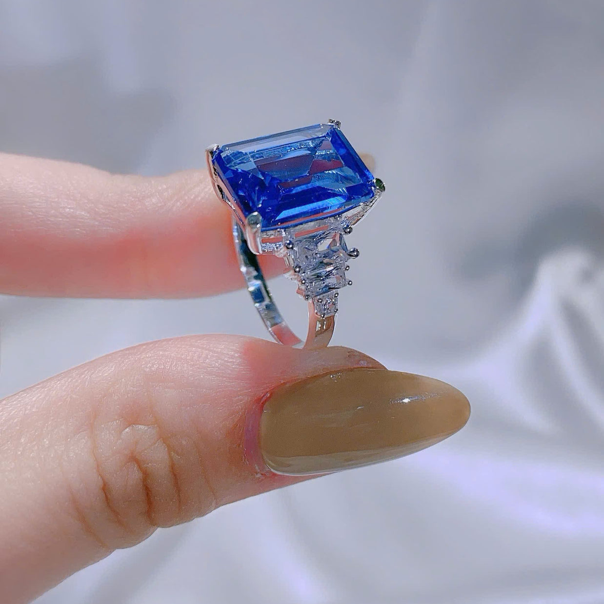 Ring with a blue gemstone held on a finger against a neutral background