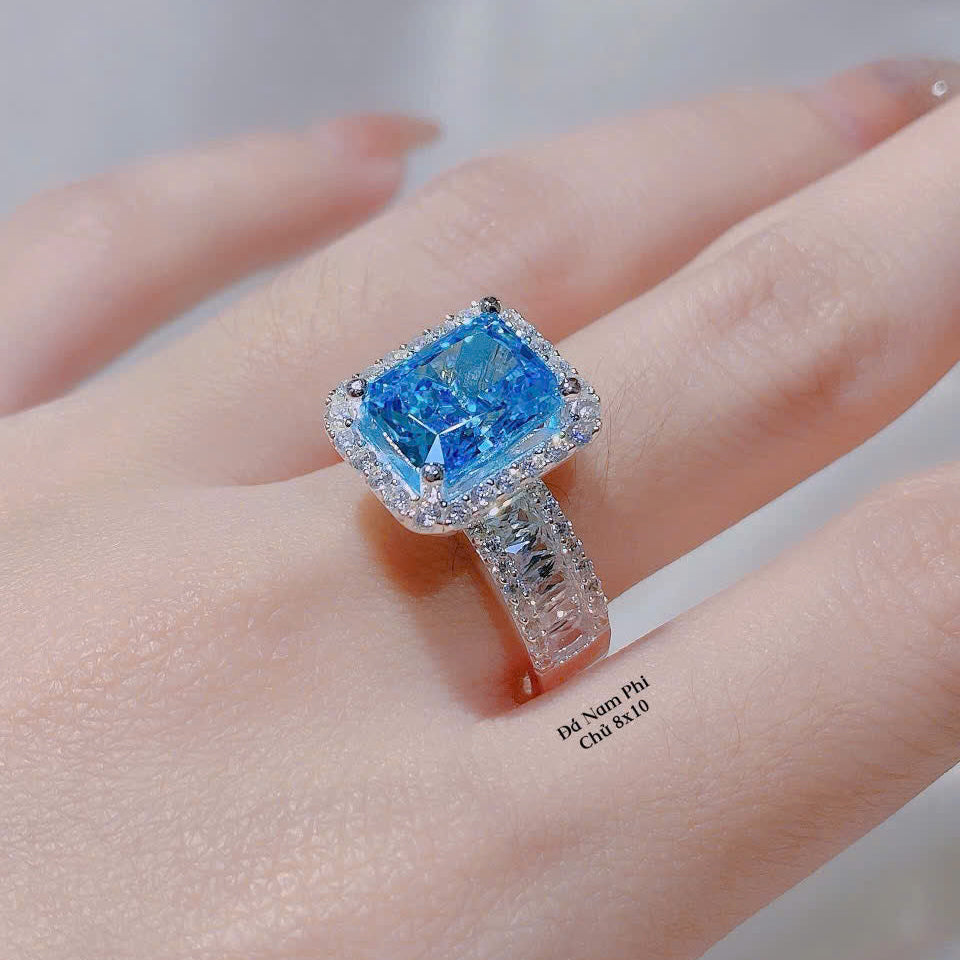 Ring with a blue gemstone on a person's finger against a neutral background