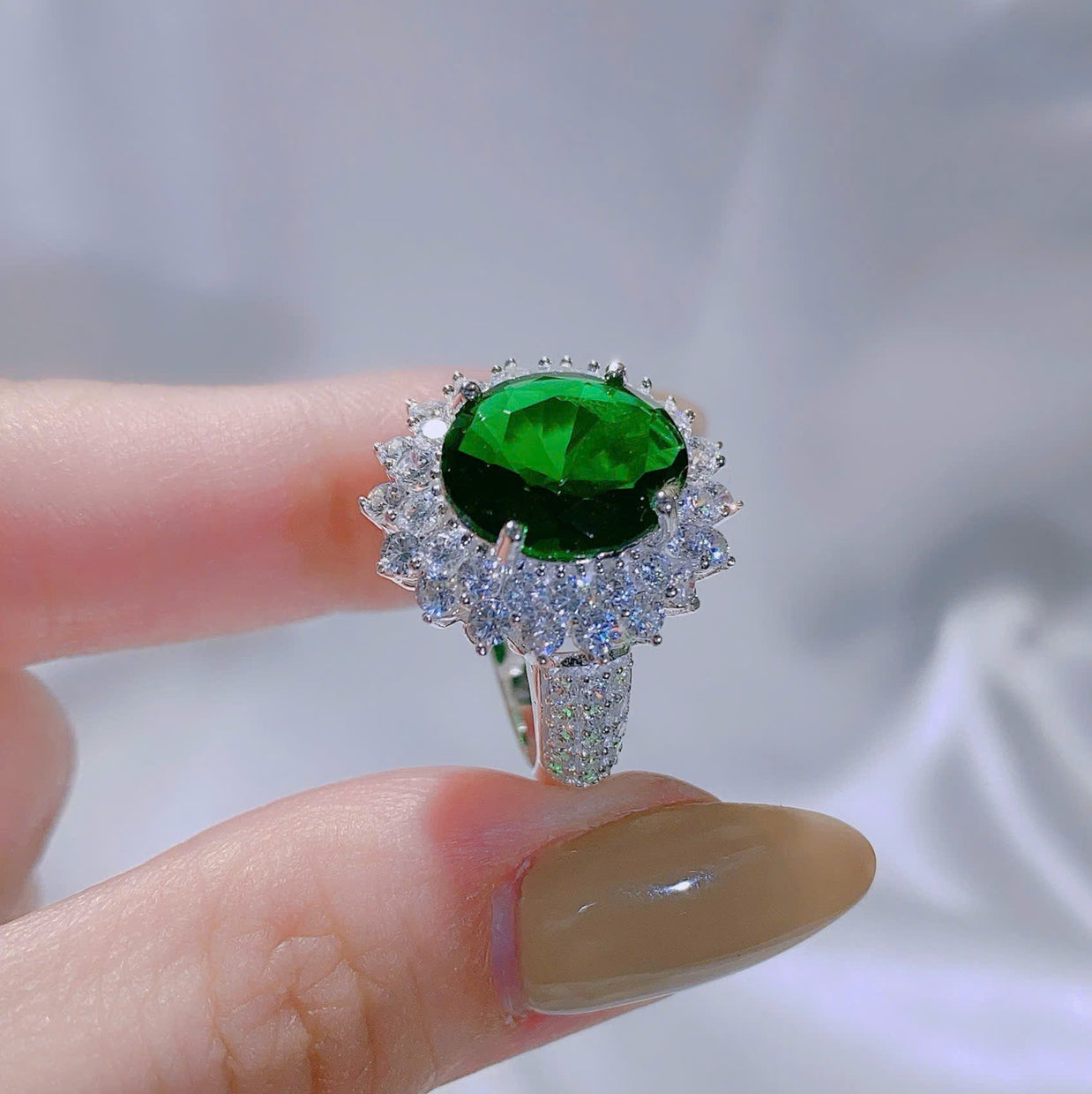 Ring with a green gemstone held by a hand against a blurred background