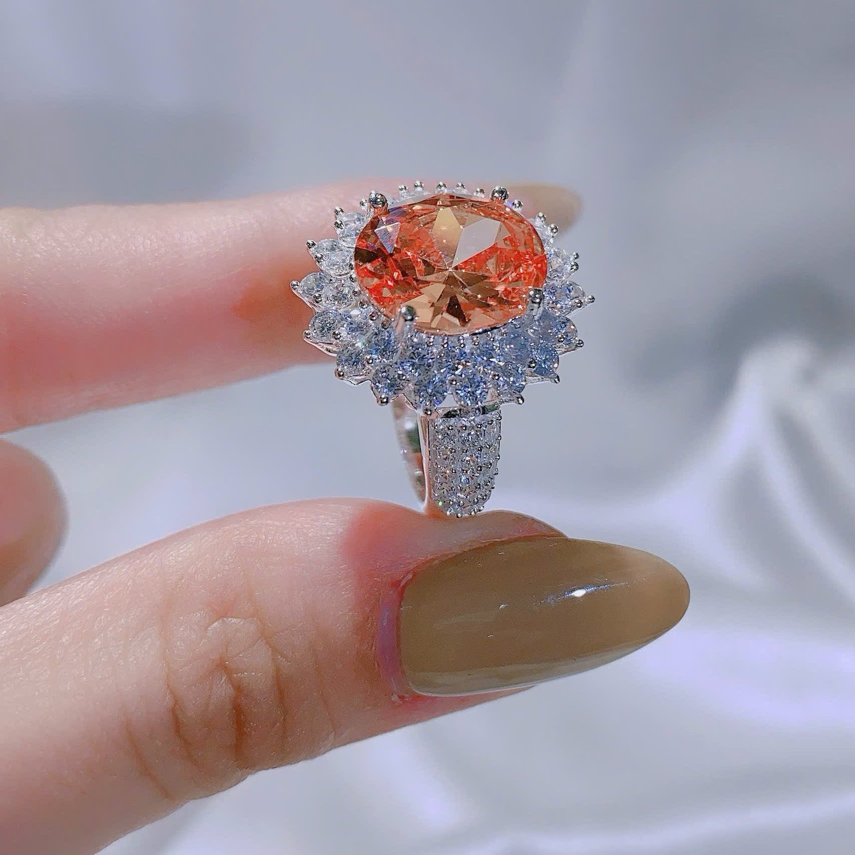 Ring with a large orange gemstone held on a finger against a neutral background