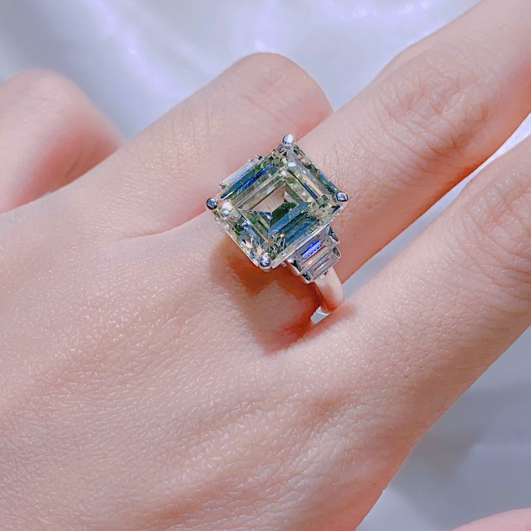 Ring with a large diamond on a person's finger against a neutral background