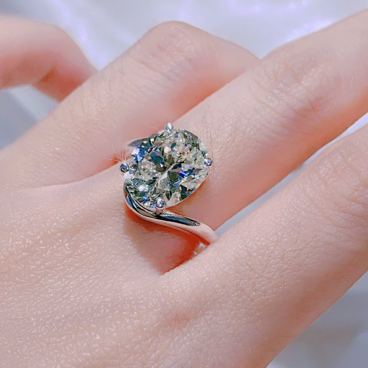 Ring with a large diamond on a person's finger against a neutral background