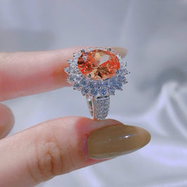 Ring with a large orange gemstone held on a finger against a neutral background