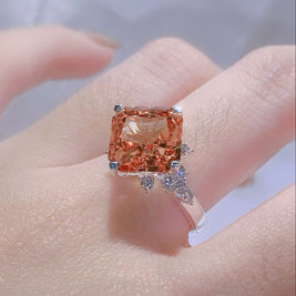 Ring with a large orange gemstone on a hand against a neutral background