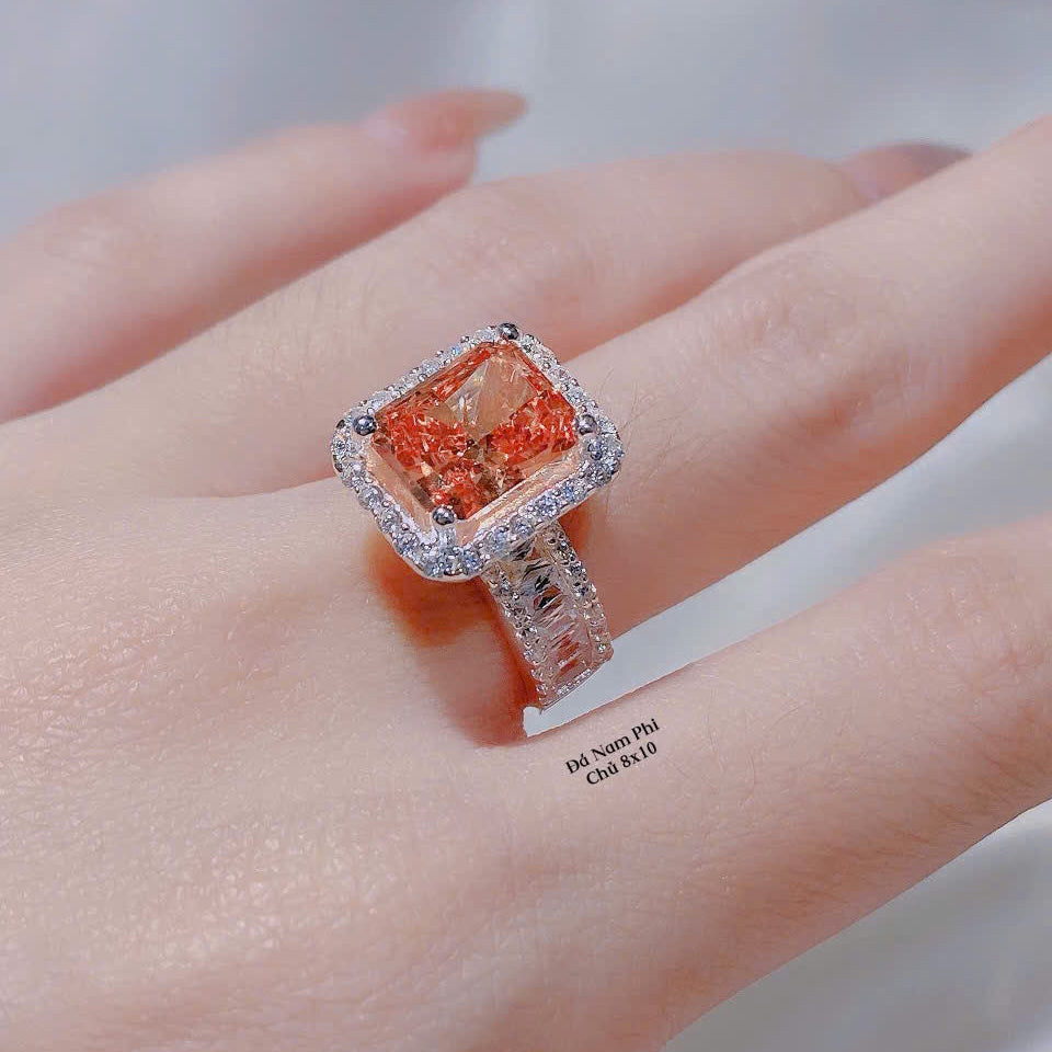 Ring with a large orange gemstone on a person's finger against a neutral background