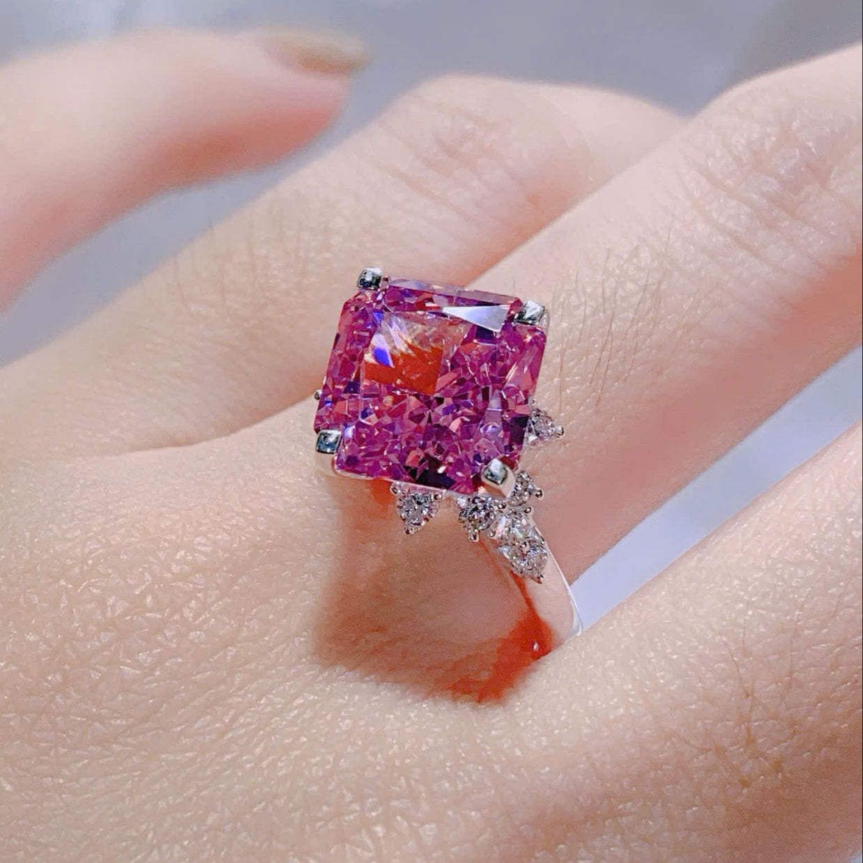 Ring with a large pink gemstone on a hand against a neutral background
