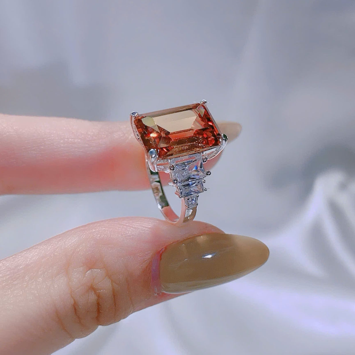Ring with a large square-cut gemstone held between fingers against a neutral background