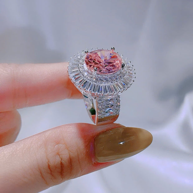 Ring with a pink gemstone held by a hand against a neutral background