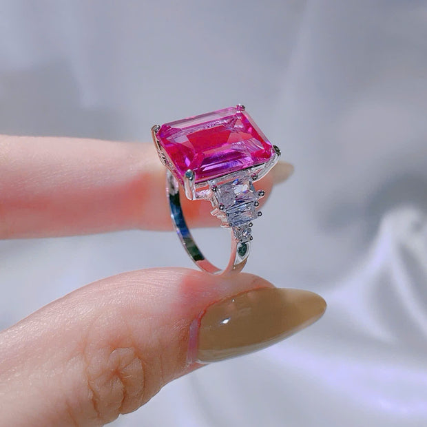 Ring with a pink gemstone held by a hand against a neutral background