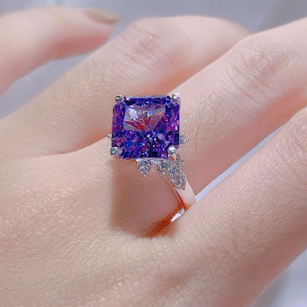 Ring with a purple gemstone on a hand against a neutral background