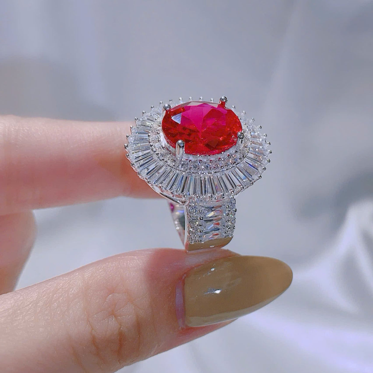 Ring with a red gemstone held on a finger against a white background
