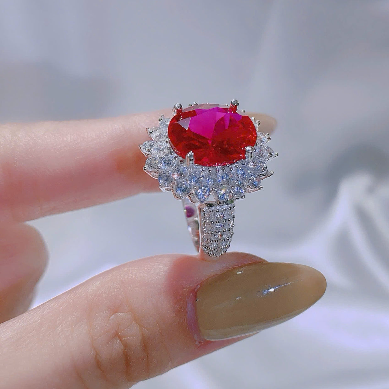Ring with a red gemstone held by a hand against a neutral background