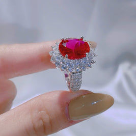 Ring with a red gemstone held by a hand against a neutral background