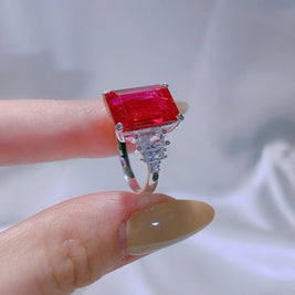 Ring with a red gemstone held on a finger against a white background